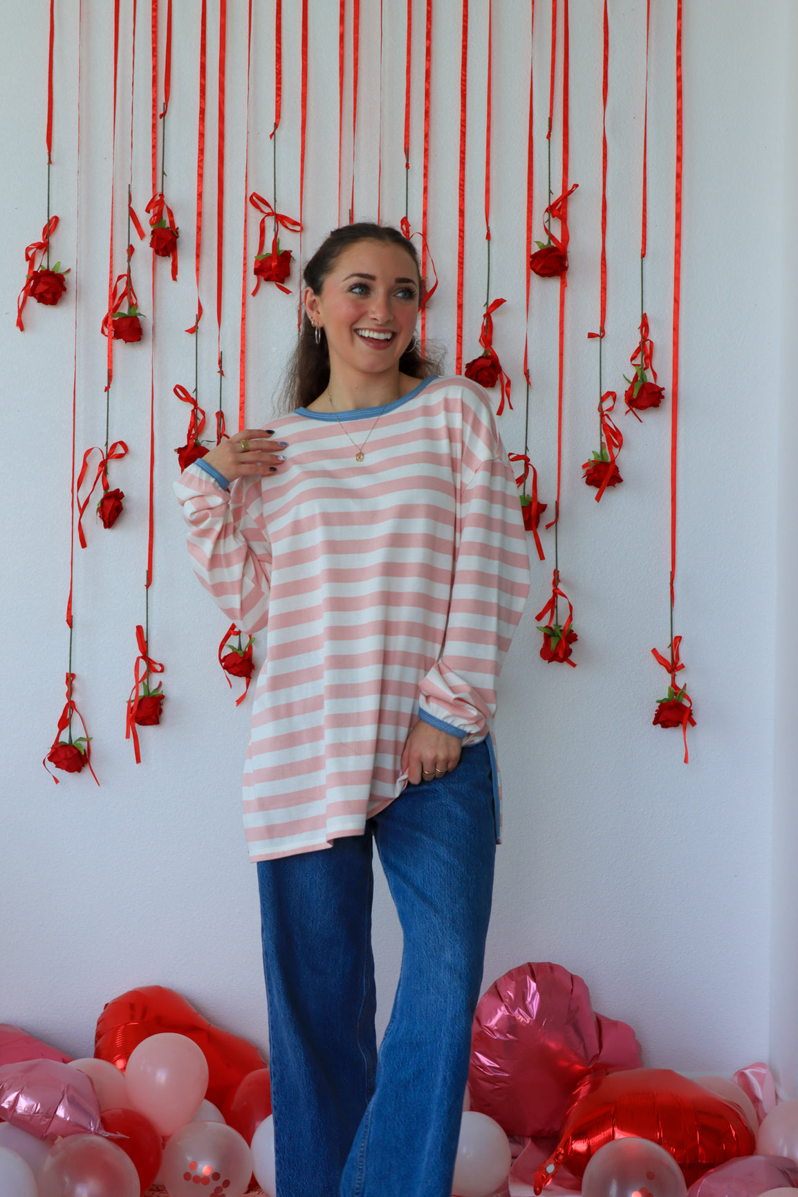 Woman standing in front of a decorative wall with red ribbons and balloons.