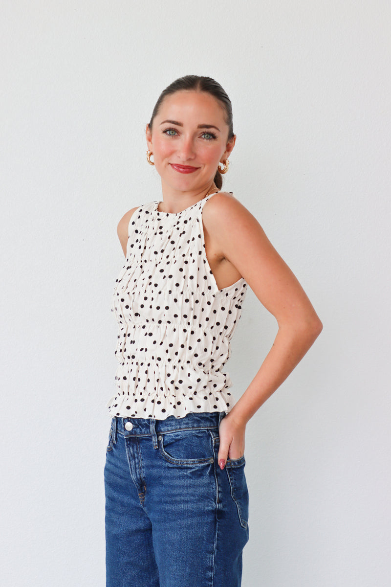 Woman wearing a polka dot top and blue jeans against a plain background
