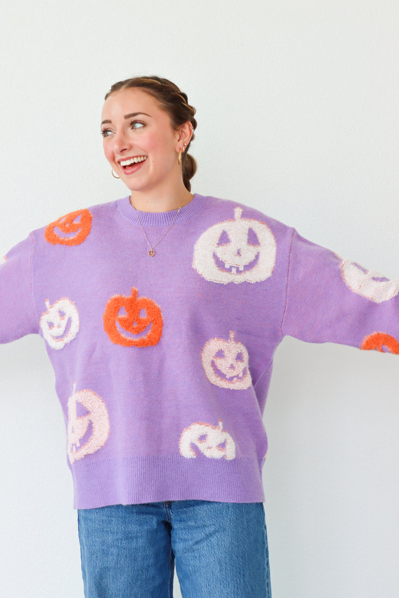 Person wearing a purple sweater with Halloween-themed pumpkins on a white background