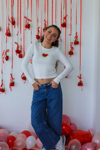 Woman posing in front of a decorative wall with red ribbons and balloons.
