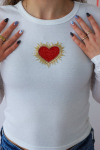 White long-sleeve shirt with a red heart and sunburst design, worn by a person.