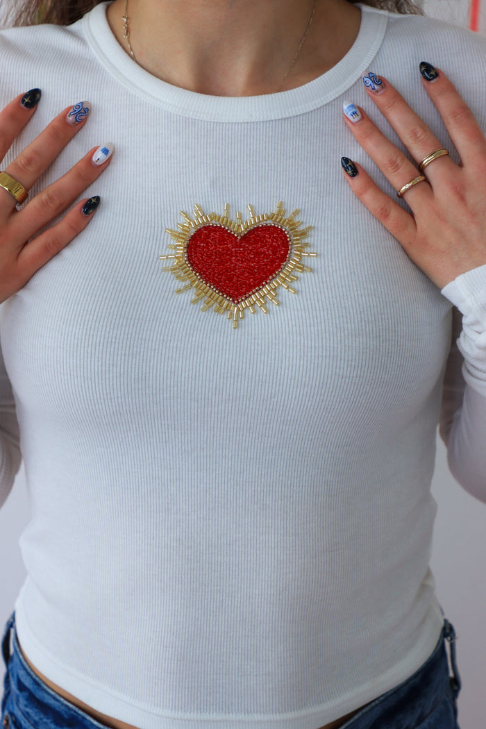 White long-sleeve shirt with a red heart and sunburst design, worn by a person.