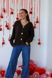 Woman in a black cardigan and blue jeans standing in front of a decorative wall with red ribbons and balloons.