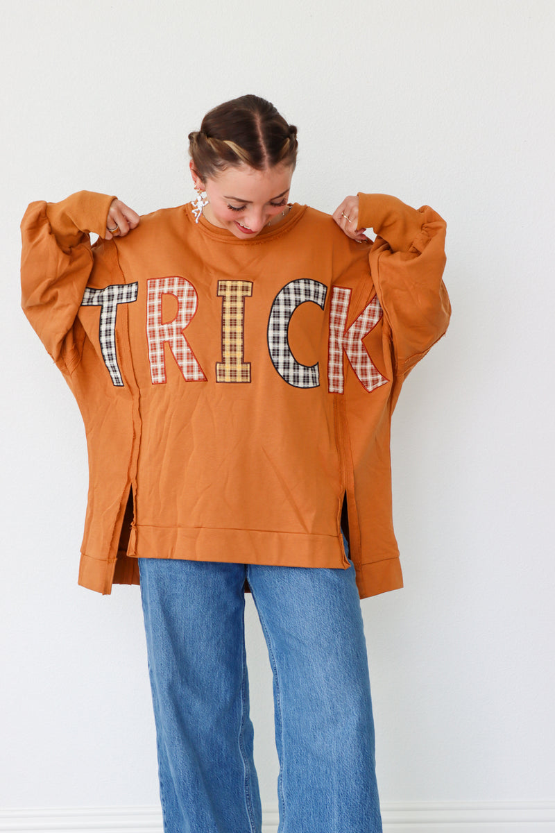 Person wearing an orange sweatshirt with 'TRICK' printed on it, standing against a white background