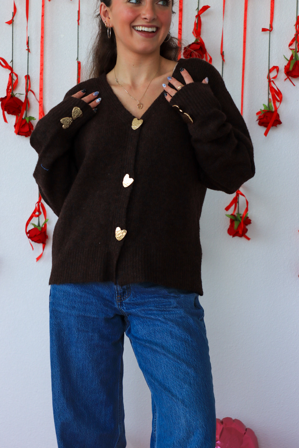 Woman wearing a black cardigan with heart buttons against a white wall with red decorations.