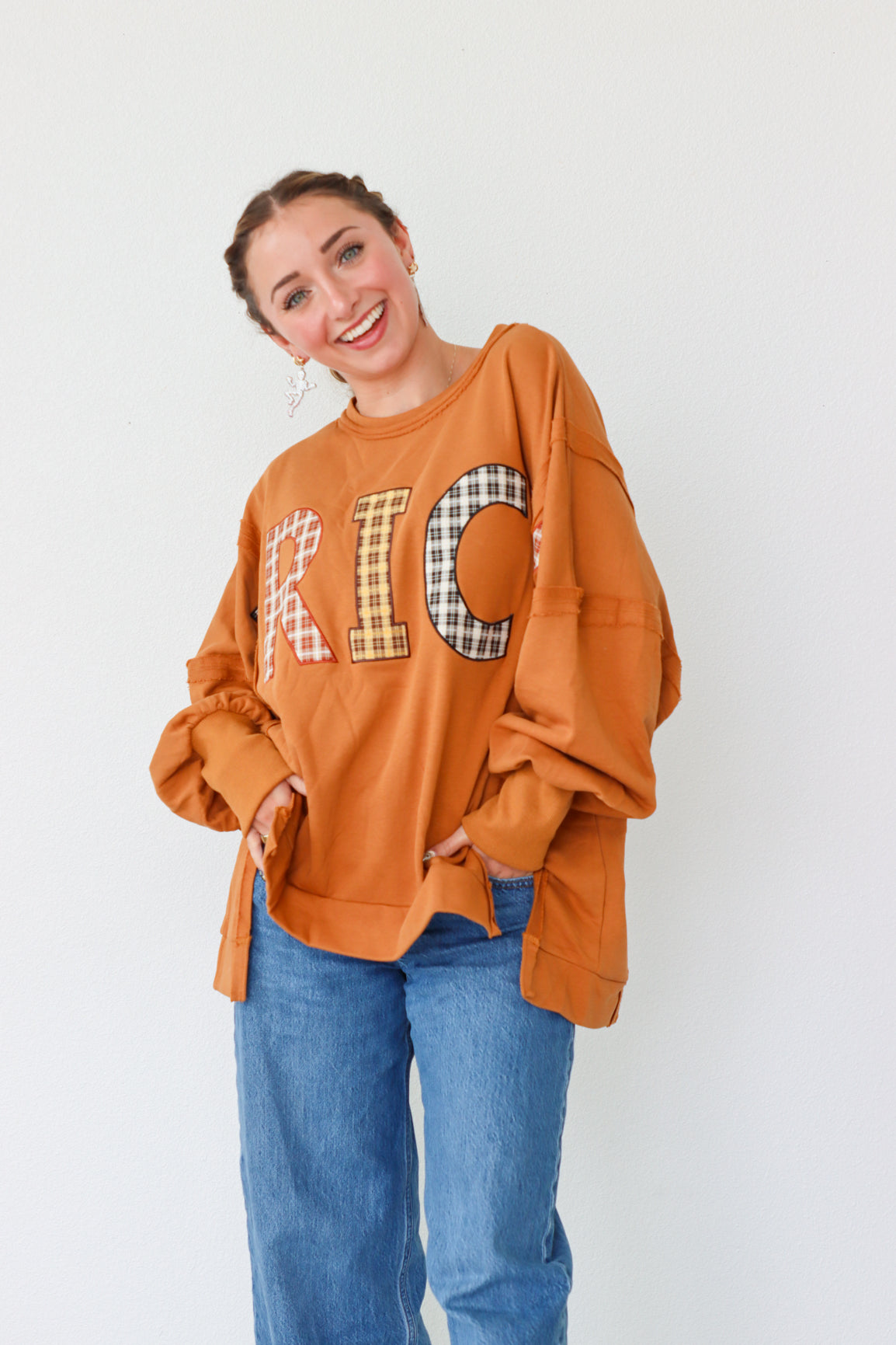 Woman wearing an orange sweatshirt with plaid lettering on a white background