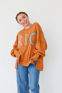 Woman wearing an orange sweatshirt with plaid lettering on a white background