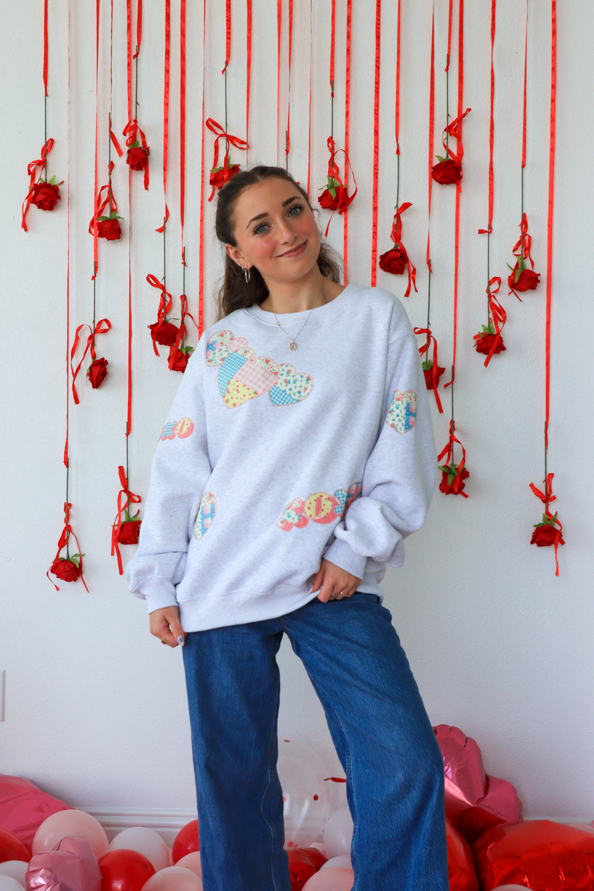 Person wearing a light blue sweatshirt with colorful patterns in front of a decorative wall with red ribbons and balloons.