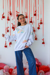 Woman wearing a light blue sweatshirt with colorful patterns in a room decorated with red ribbons and balloons.