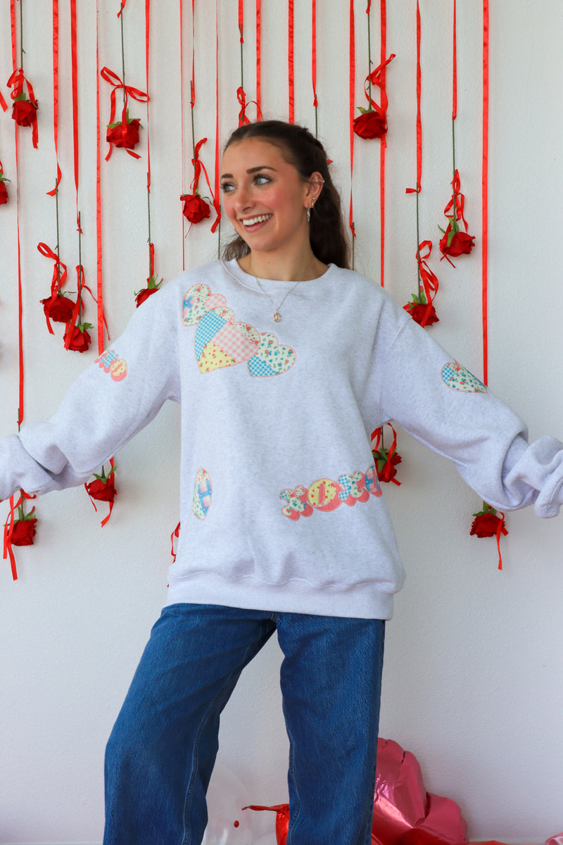 Person wearing a light gray sweatshirt with colorful patterns in front of a decorative wall with red ribbons and flowers.