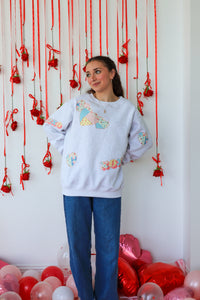 Woman wearing a colorful sweater with heart designs in front of a decorative wall with red ribbons and balloons.