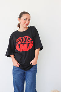Woman wearing a black t-shirt with red 'Spooky' design and blue jeans on a white background