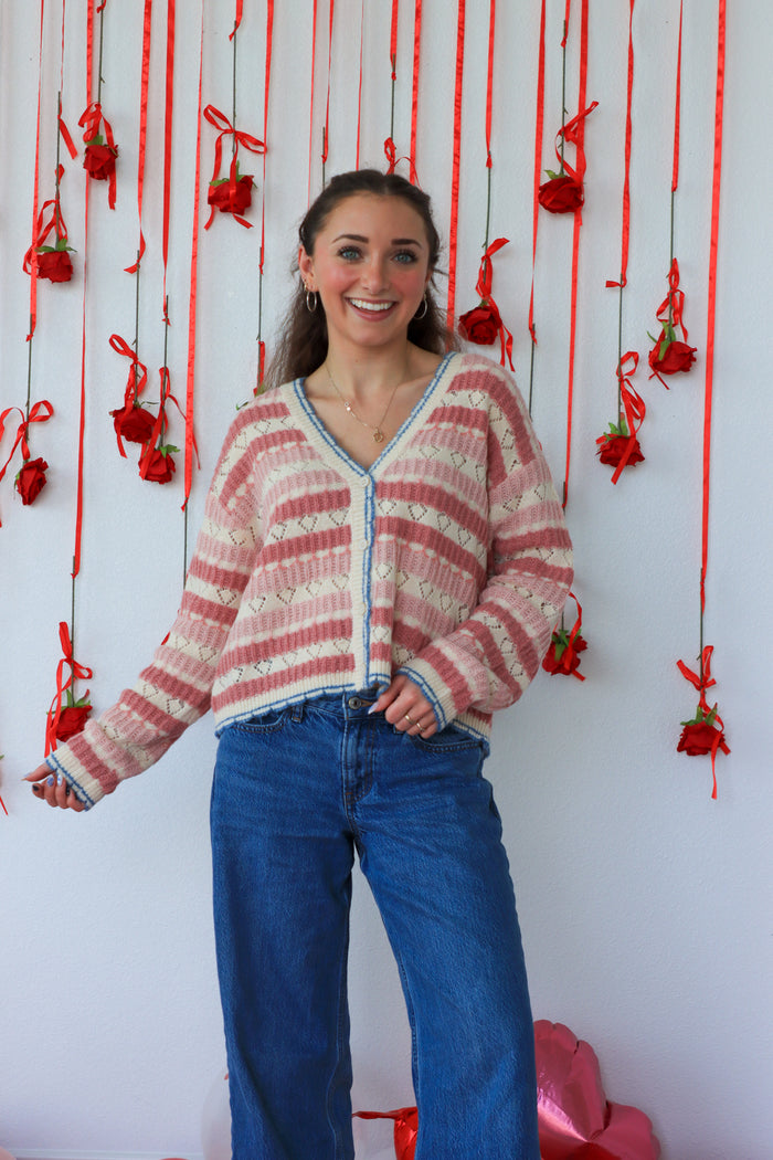 Woman wearing a striped sweater and blue jeans standing in front of a wall with red decorations.