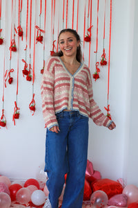 Woman wearing a striped sweater and blue jeans standing in front of a decorative wall with red ribbons and balloons.