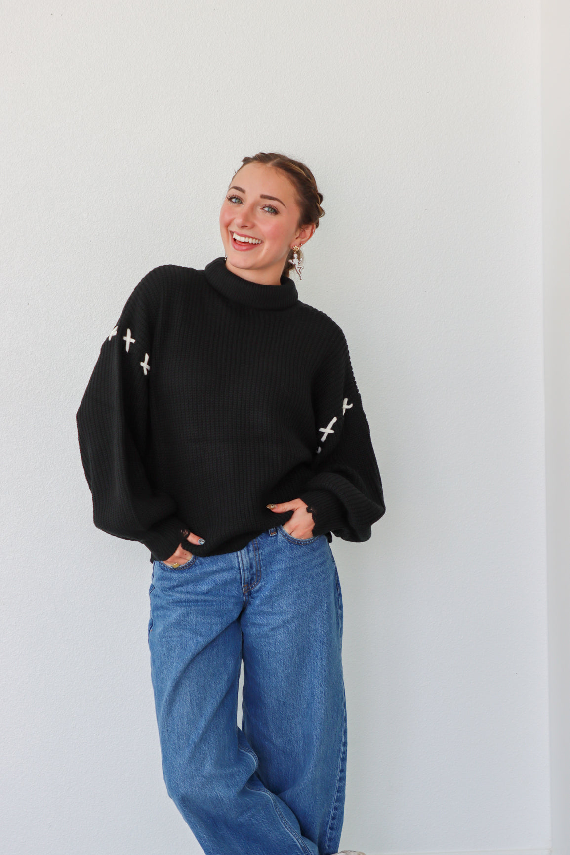 Person wearing a black sweater with white patterns and blue jeans against a plain background