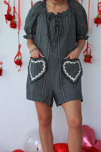 Person wearing a black and white checkered romper with heart pockets against a white background with red decorations.