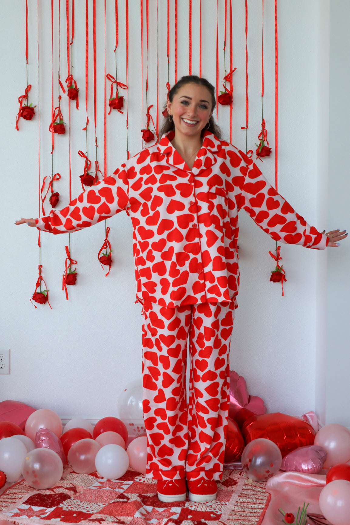 Person wearing a red and white heart-patterned onesie in a decorated room with balloons and hanging decorations.