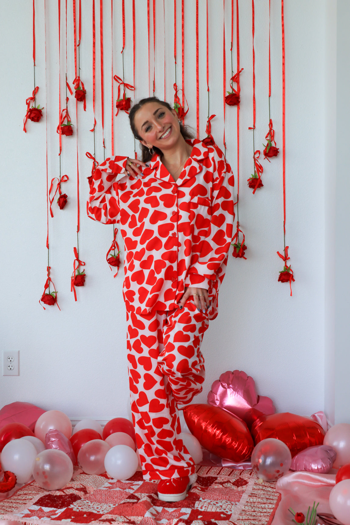 Person wearing a red and white heart-patterned onesie in a room decorated with red and pink balloons.