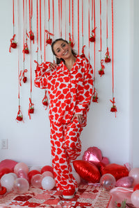 Person wearing a red and white heart-patterned onesie in a room decorated with red and pink balloons.