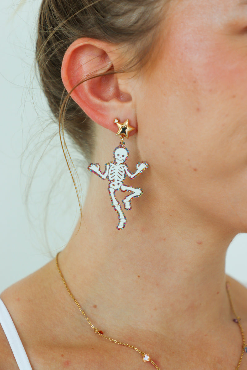 Skeleton-shaped earrings worn by a person with a plain background