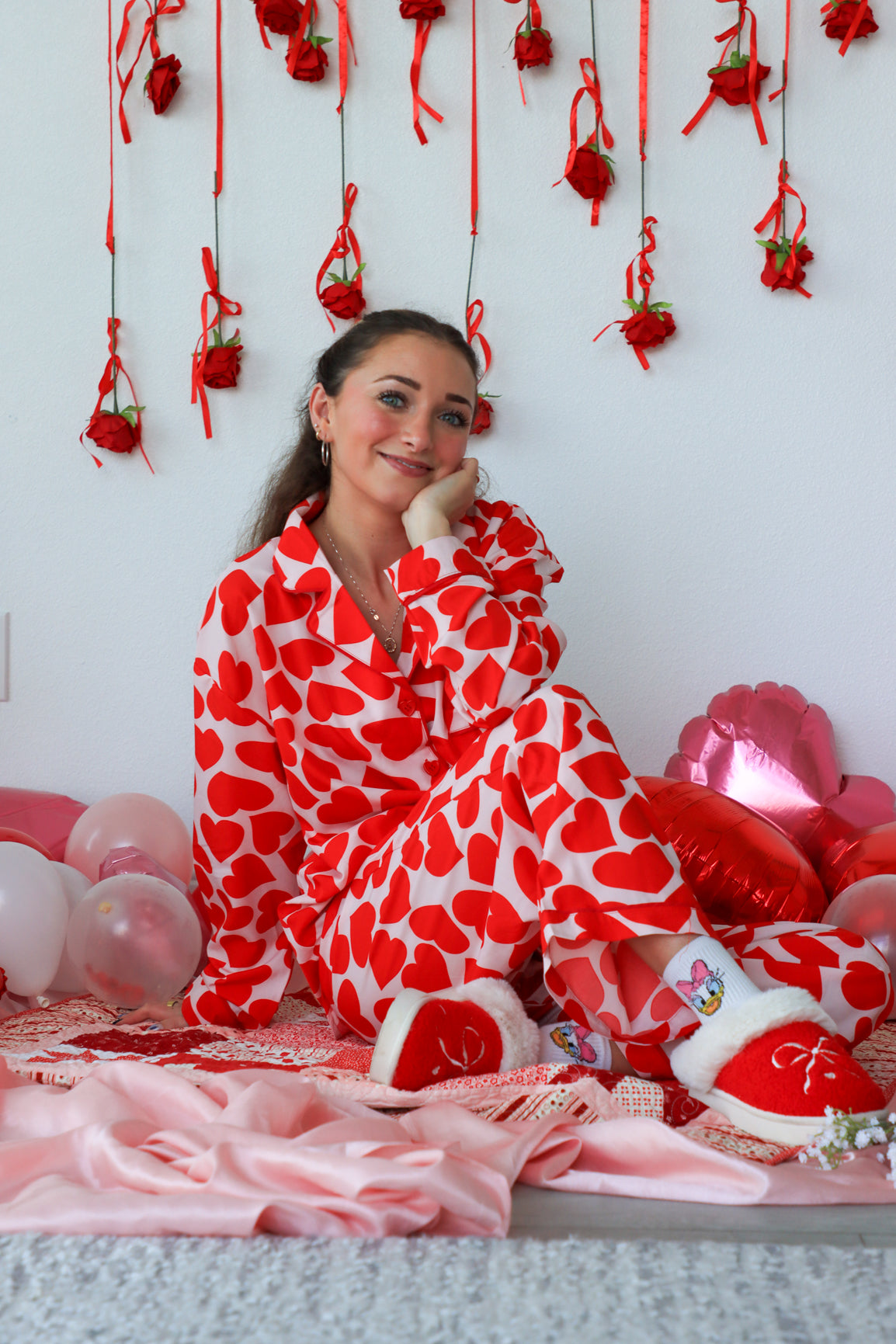 Woman in a red and white heart-patterned onesie surrounded by Valentine's Day decorations.