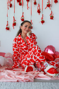 Woman in a red and white heart-patterned onesie surrounded by Valentine's Day decorations.