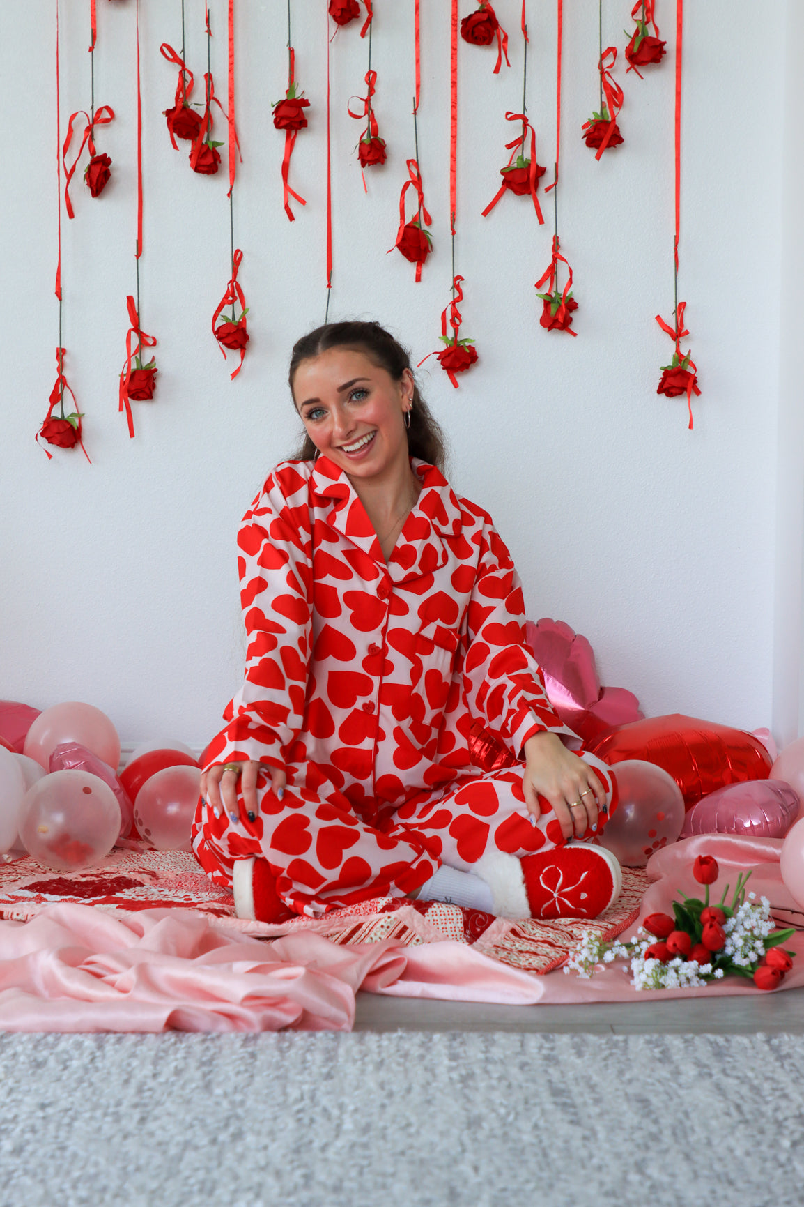 Woman in a red and white heart-patterned robe sitting on a floor decorated with red ribbons and balloons.