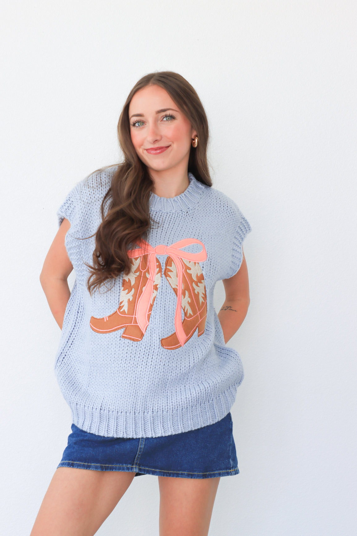 Woman wearing a light blue sweater with orange boots design against a white background