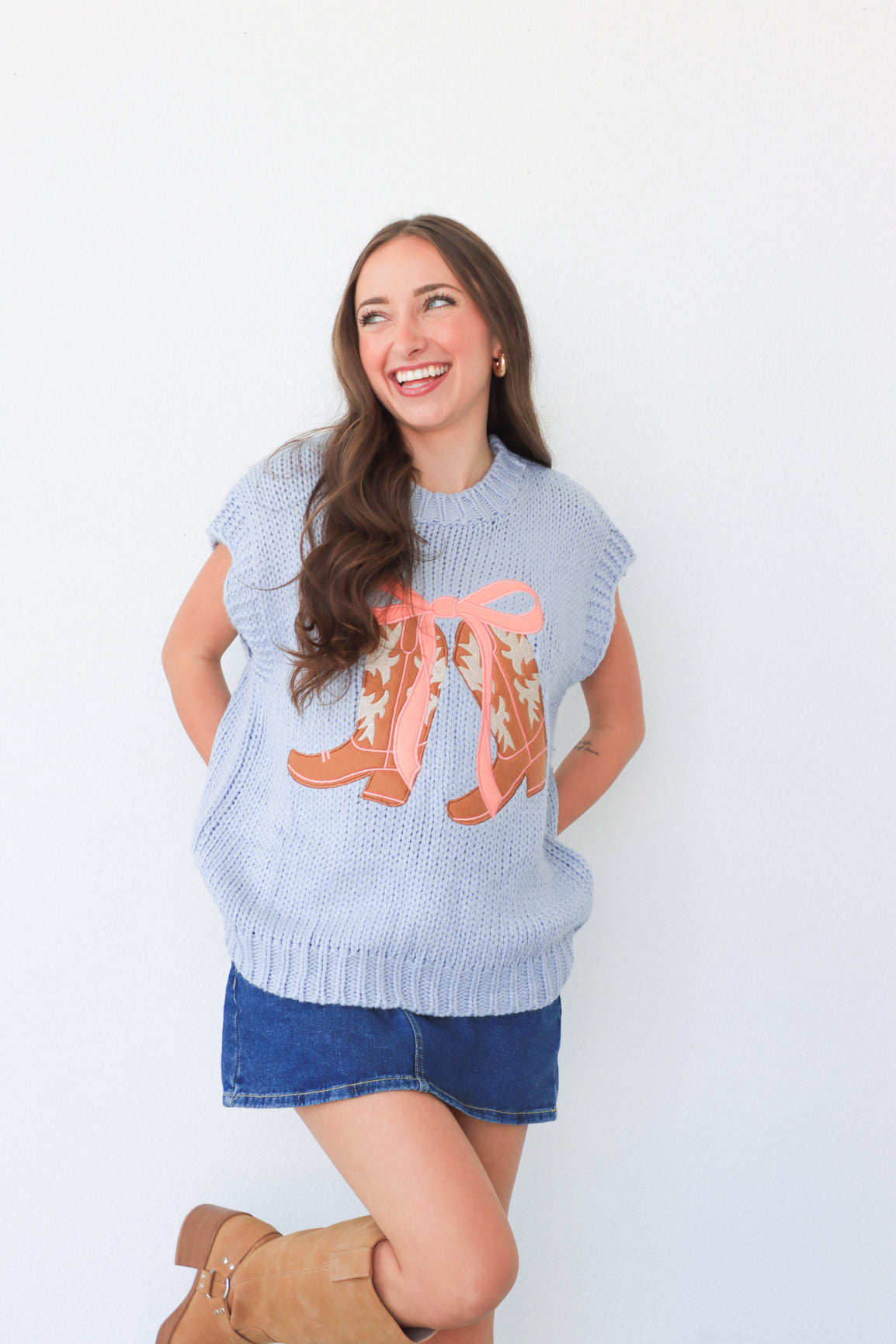 Woman wearing a light blue sleeveless sweater with pink boots design on a white background