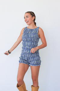 Woman wearing a blue checkered romper with brown boots against a white background