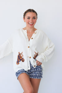 Woman wearing a white cardigan with horse embroidery and blue checkered shorts on a white background