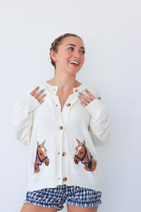 Woman wearing a white cardigan with horse designs and blue shorts on a white background