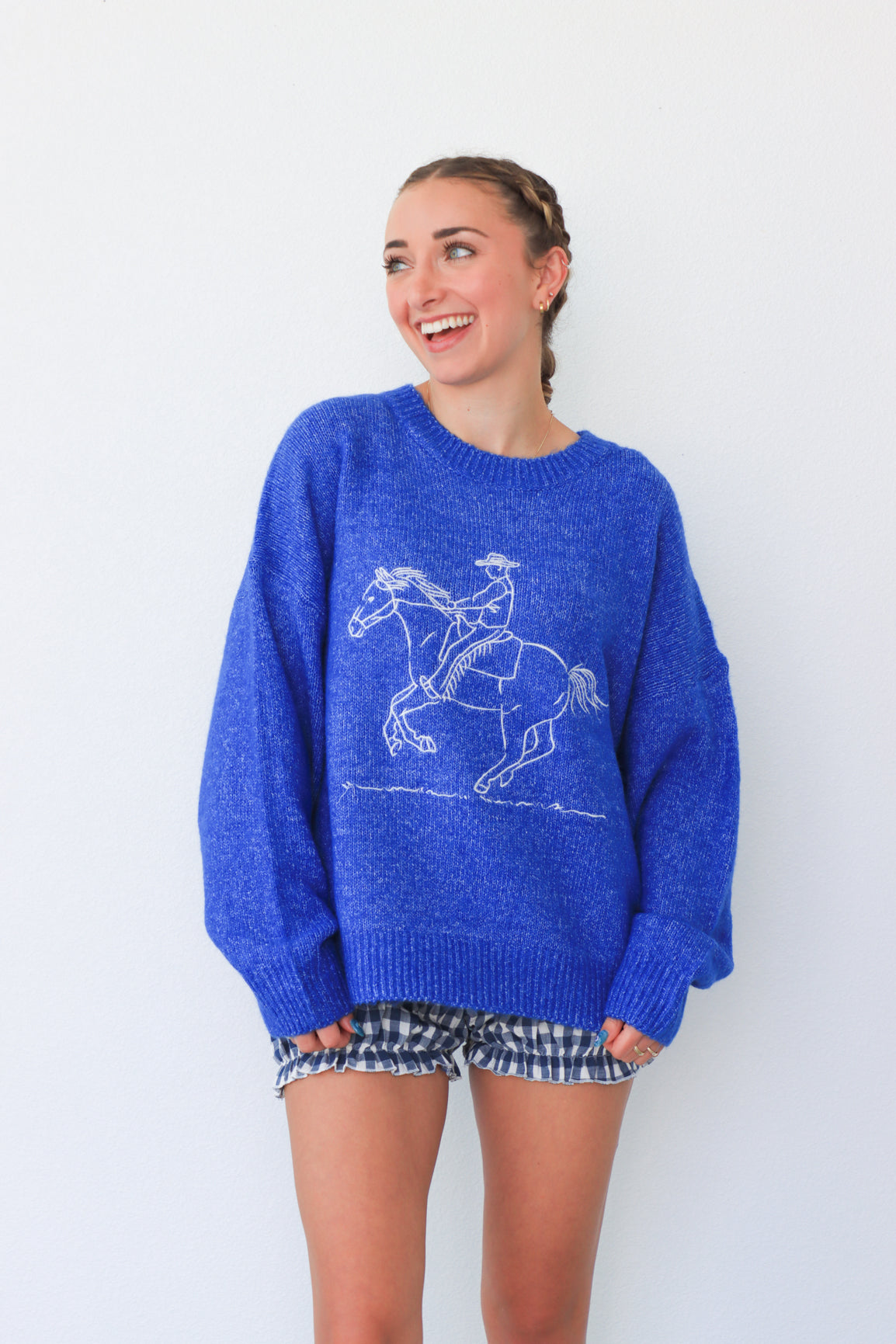 Woman wearing a blue sweater with a horse design against a white background
