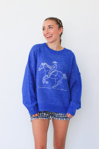 Woman wearing a blue sweater with a horse design against a white background