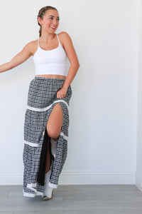 Woman wearing a white tank top and plaid skirt with a high slit, standing against a plain background.