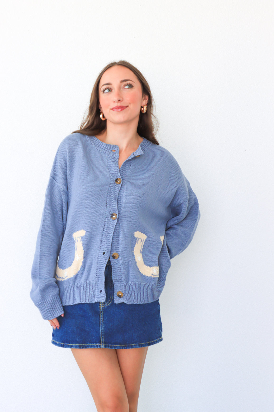 Woman wearing a blue cardigan with horse shoe designs on a white background
