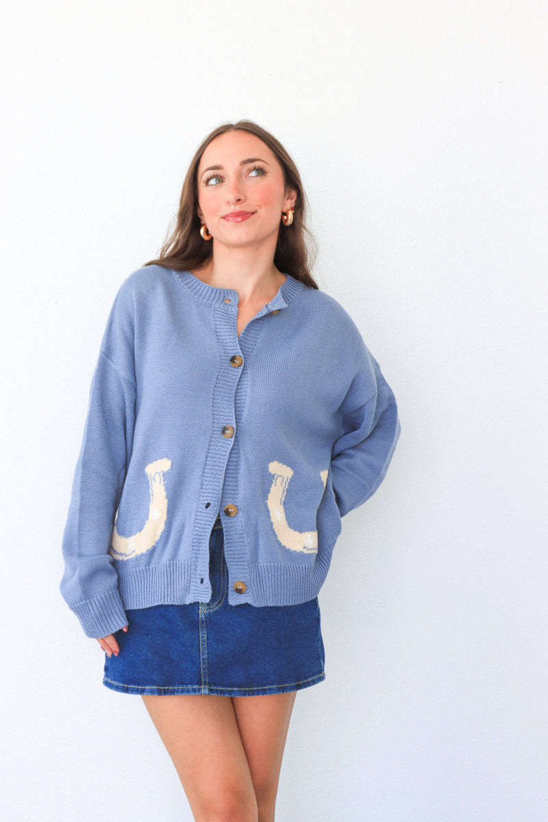 Woman wearing a blue cardigan with horse shoe designs on a white background