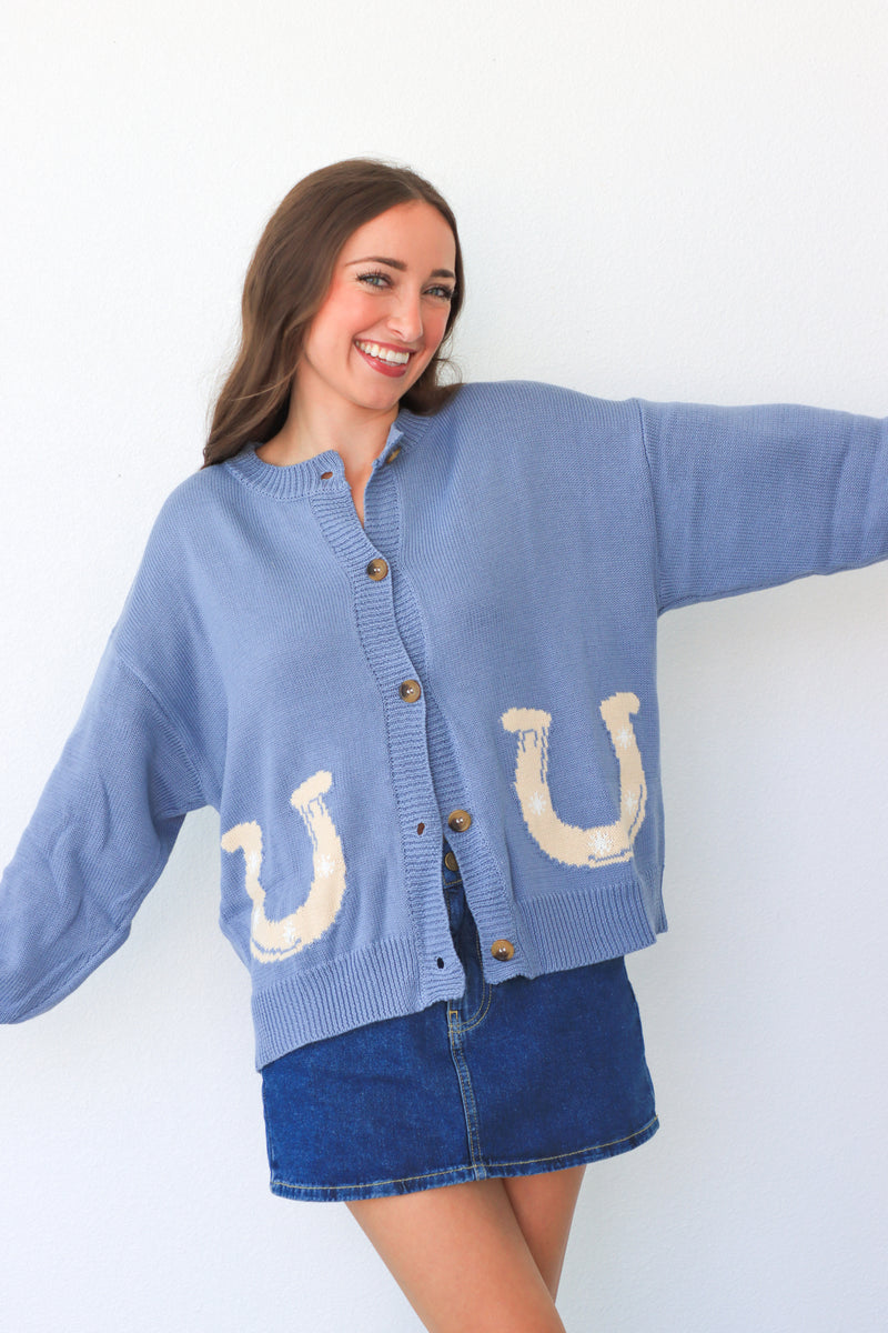 Woman wearing a blue cardigan with horse shoe designs on a white background