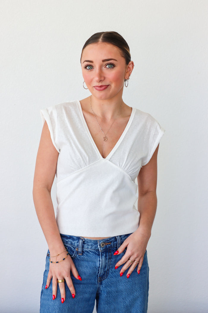 Woman wearing a white top and blue jeans against a plain background