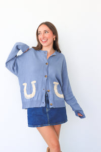 Woman wearing a blue cardigan with horse shoe patterns on a white background