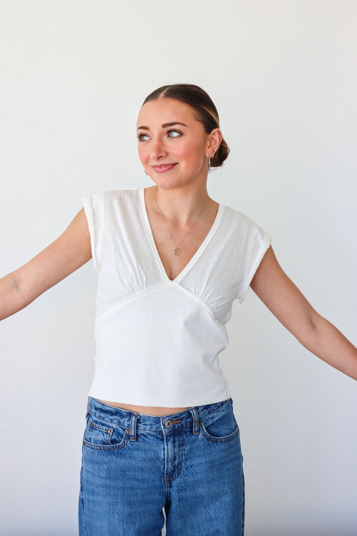Woman wearing a white top and blue jeans against a plain background