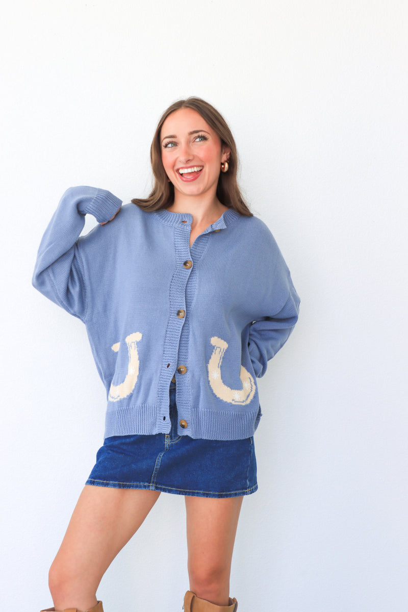 Woman wearing a blue cardigan with horse shoe designs on a white background