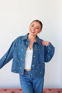 Woman wearing a blue denim jacket with colorful buttons against a white background