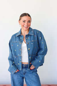 Person wearing a blue denim jacket with colorful buttons against a white background