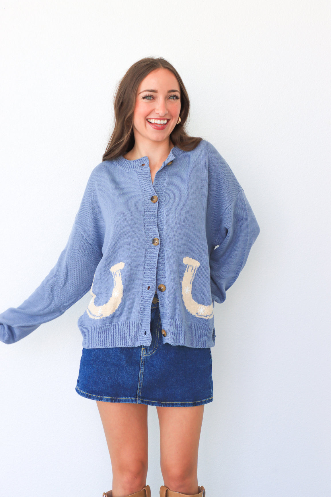 Woman wearing a blue cardigan with horse shoe designs on a white background