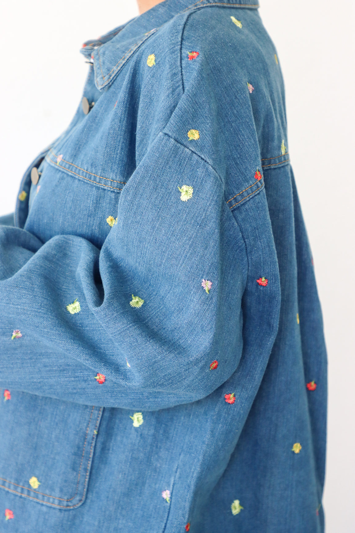 Blue denim jacket with colorful embroidered patterns on a white background