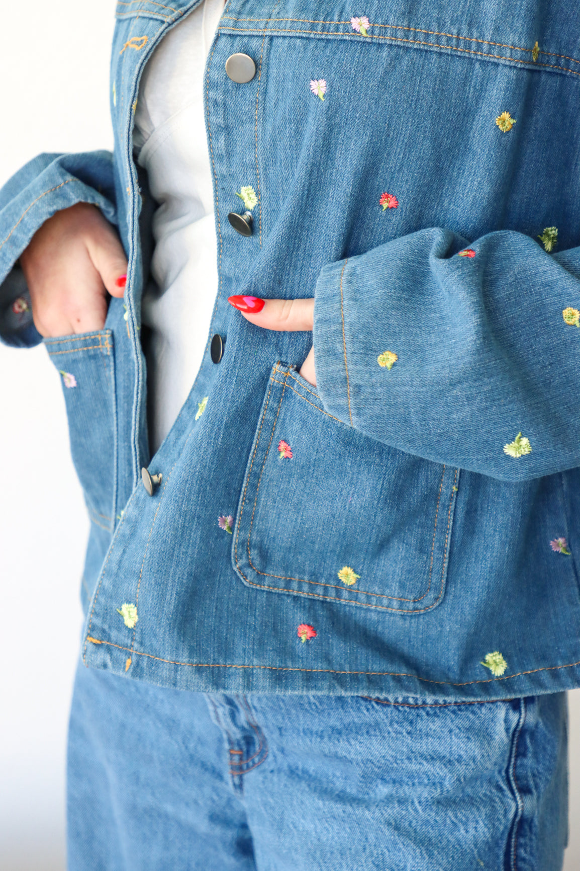 Close-up of a blue denim jacket with floral embroidery on a plain background
