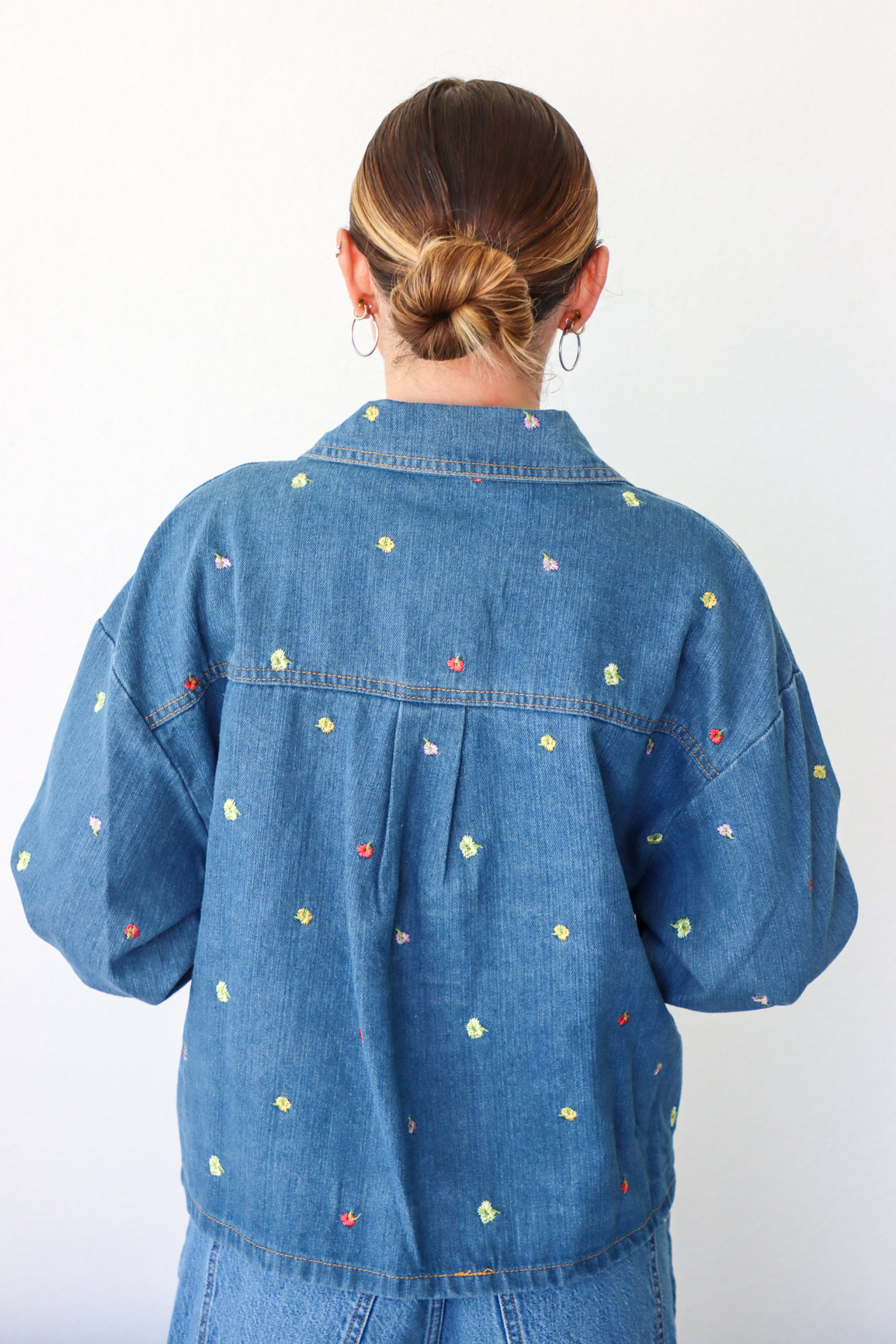 Person wearing a blue denim jacket with colorful floral patterns on a white background