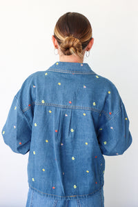 Person wearing a blue denim jacket with colorful floral patterns on a white background