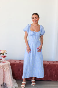 Woman wearing a blue checkered dress standing in a room with a pink couch and table.